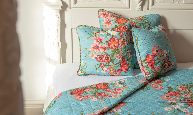 A romantic bed made up with pillows and a bedspread, featuring blue with pink and red flowers
