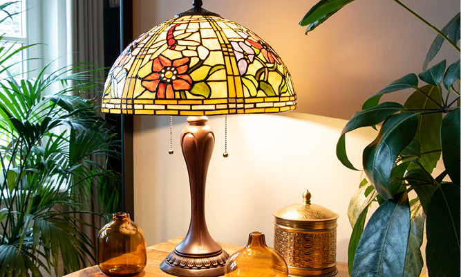 Une lampe de table Tiffany vintage avec des fleurs intégrées dans l'abat-jour en verre, et des vases bruns disposés autour de la lampe