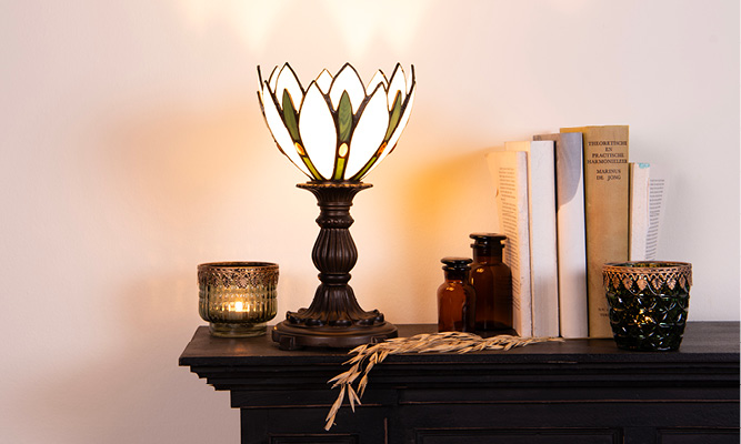 A vintage Tiffany table lamp, brown bottles, books, and green tealight holders on a black mantelpiece