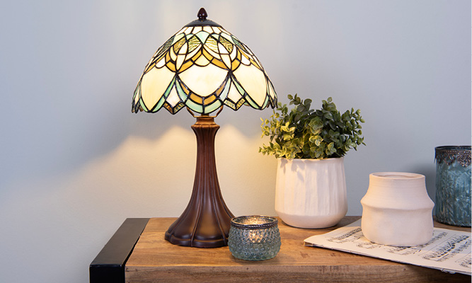 Una lampada da tavolo Tiffany che assomiglia a una ninfea su una credenza industriale con vasetti per fiori bianchi eleganti e portacandele blu