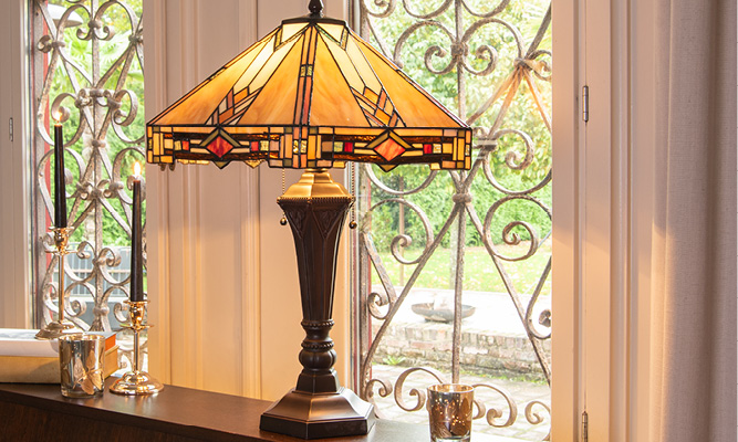 An Art Deco New York Tiffany table lamp on a wooden piano with silver candle holders and black candles