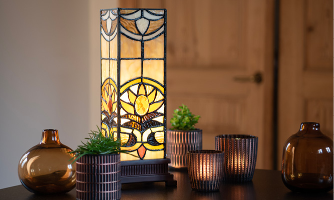 Una lampada da tavolo Tiffany rettangolare con un sole incorporato su un piano di lavoro, circondata da portacandele