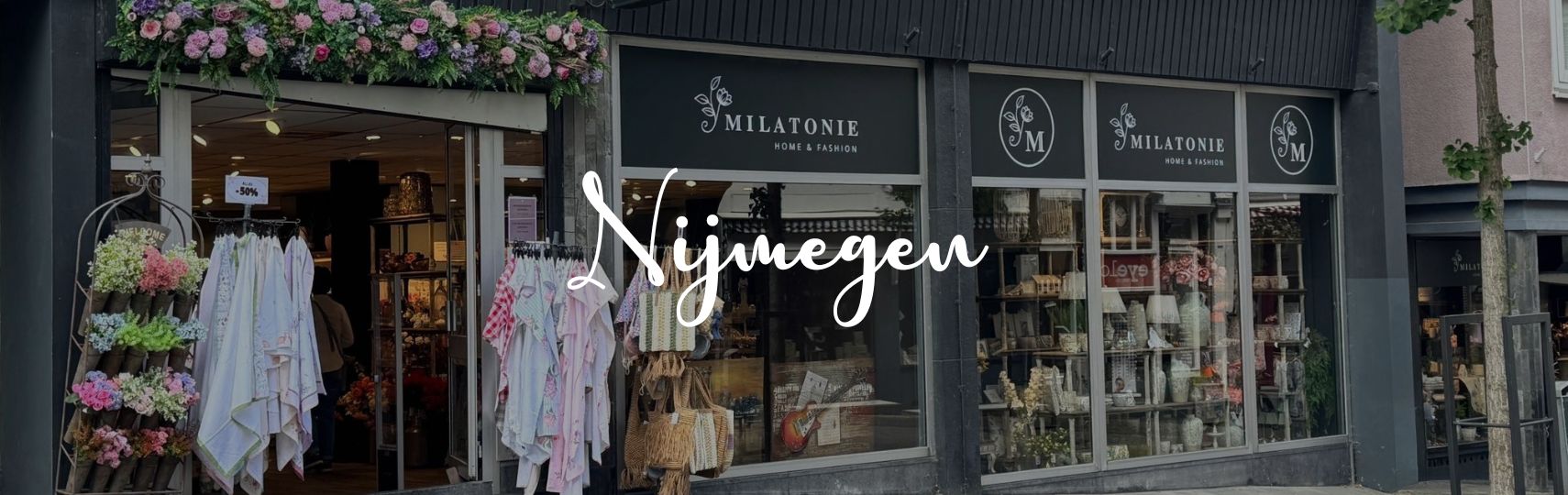 Das Milatonie-Geschäft in Nijmegen fällt auf durch einen farbenfrohen Blumenbogen und eine vielfältige Auswahl an Textilien, Taschen und Wohnaccessoires. Innen herrscht eine warme, einladende Atmosphäre.
