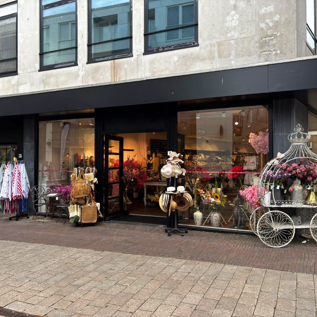La facciata di Milatonie a Maastricht è decorata con ghirlande di fiori rosa. In vetrina ci sono decorazioni d’interni suggestive con elementi naturali come piante e rattan.