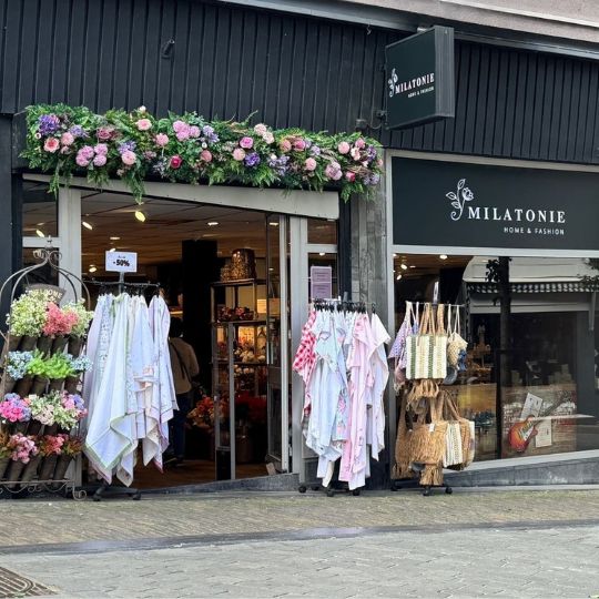De Milatonie-winkel in Nijmegen valt op met een kleurrijke bloemenboog en een gevarieerd aanbod aan textiel, tassen en woonaccessoires. Binnen heerst een warme, sfeervolle ambiance.