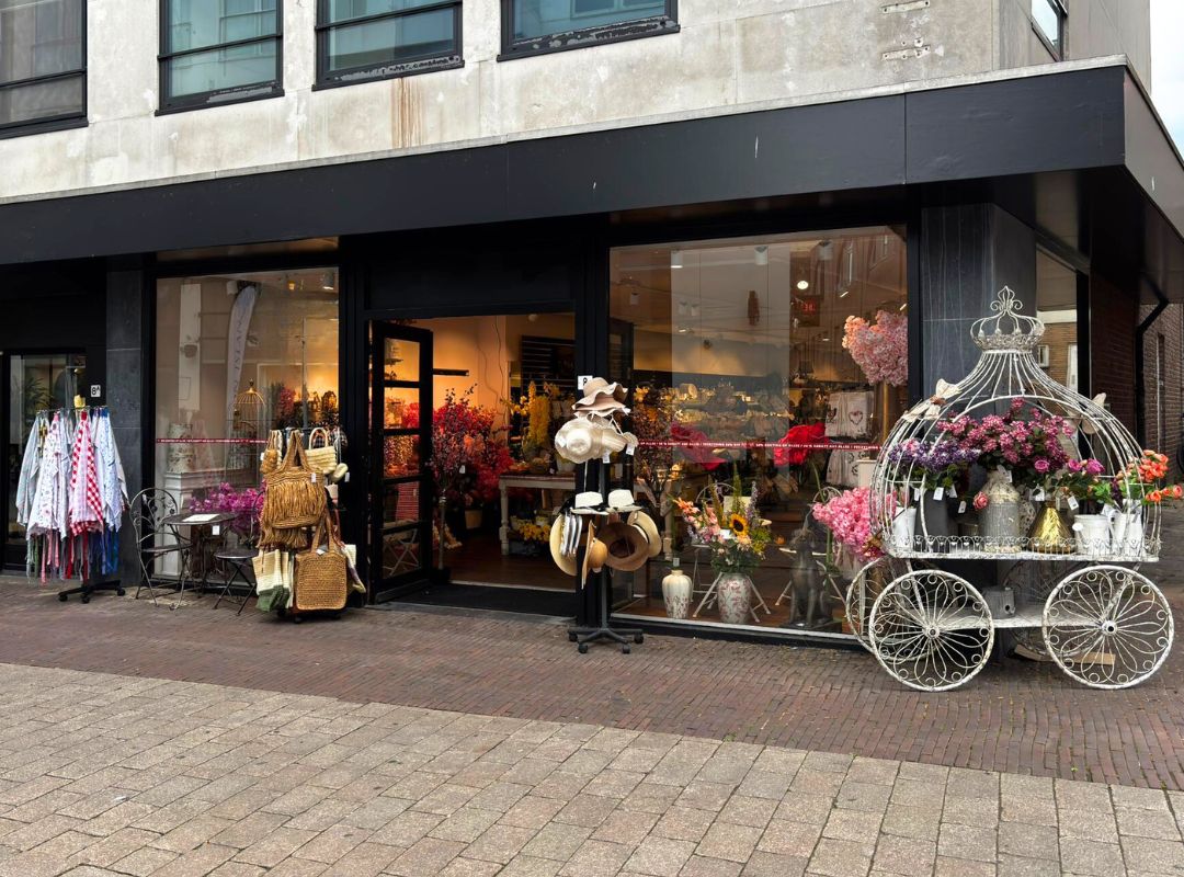 De etalage van Milatonie in Venlo is uitbundig versierd met prachtige paarse bloementrossen die over de ingang hangen. Binnen zie je een sfeervolle winkel vol woondecoratie en cadeauartikelen.