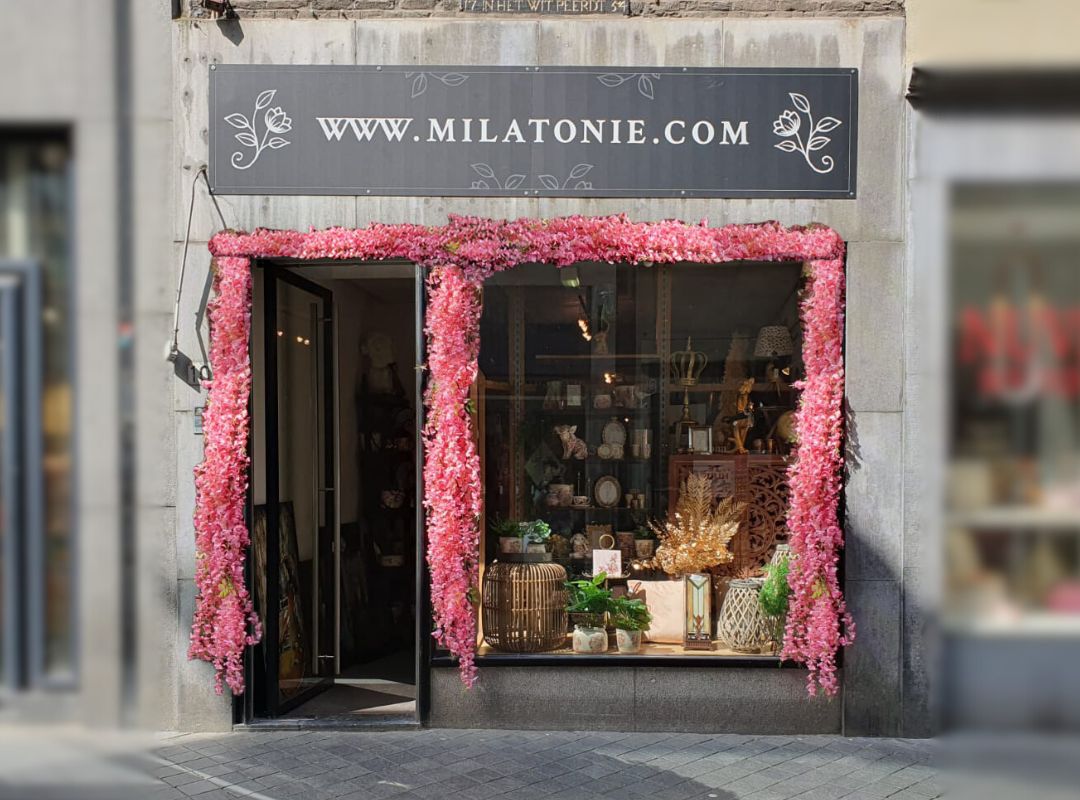 De gevel van Milatonie in Maastricht is versierd met roze bloemenslingers. In de etalage staan sfeervolle woondecoraties met natuurlijke elementen zoals planten en rotan.