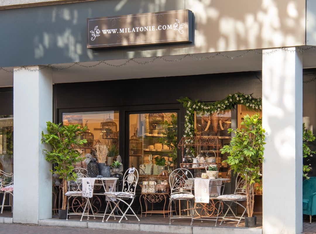 De Milatonie-winkel in Roermond straalt rust uit met zachte decoratie, witte tuinmeubels en veel groen. Door de ramen zie je een gevarieerd aanbod aan woonaccessoires.
