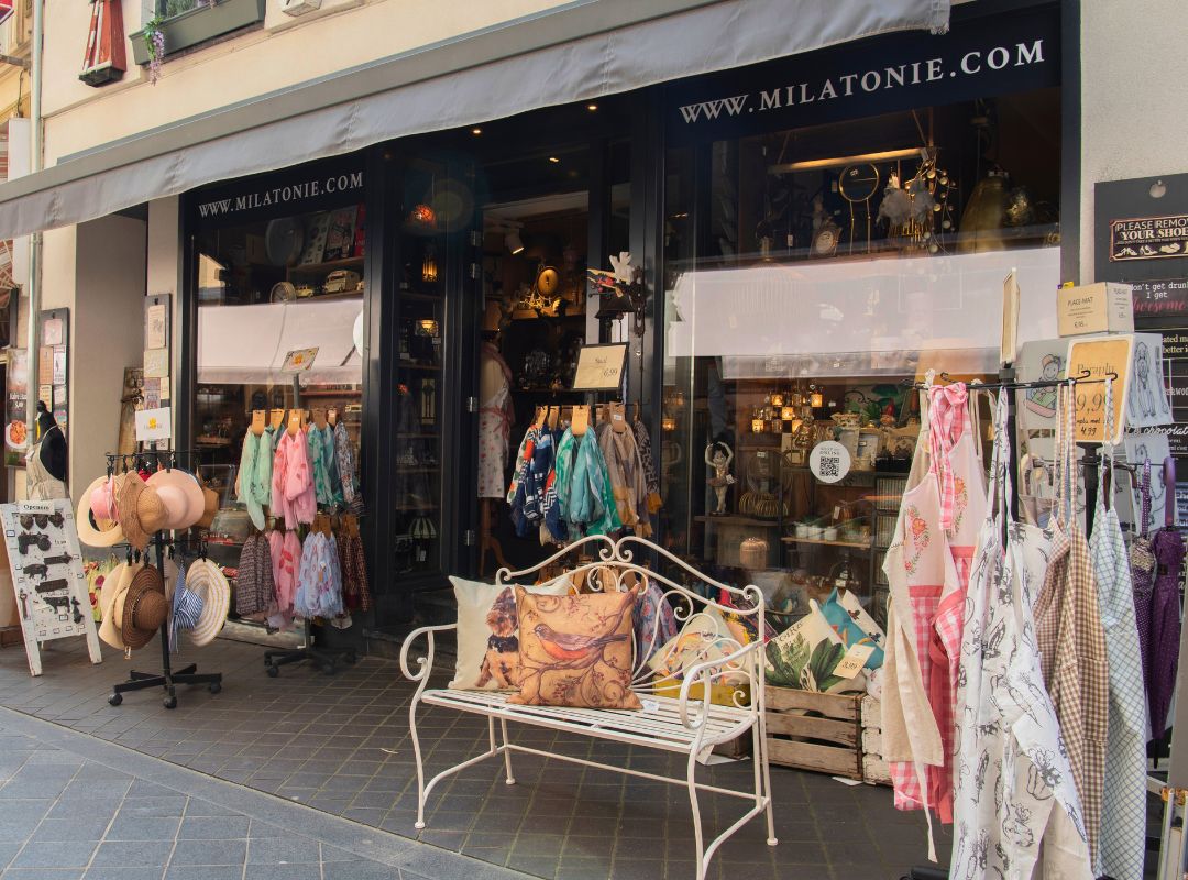 De winkel van Milatonie in Valkenburg heeft een uitnodigende etalage met kleurrijke kleding, hoeden en sfeervolle verlichting. Het straalt een gezellige, ambachtelijke sfeer uit.