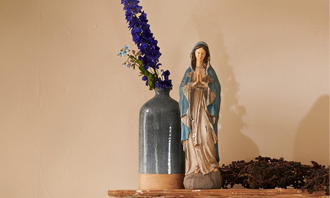 Een donkerblauwe vaas met een lavendel erin en een maria beeld ernaast