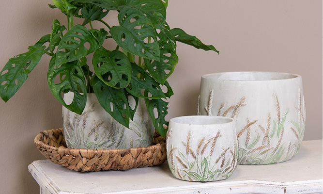 Tre vasi per fiori in pietra con fiori di segale incorporati nel motivo, e uno è posizionato su un vassoio di vimini