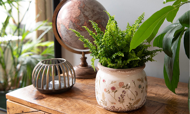A wooden sideboard with a colorful plant pot, a gold tealight holder, and a vintage globe