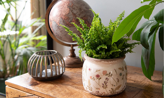 Un buffet en bois avec un pot de fleurs coloré, un porte-bougie doré et un globe vintage