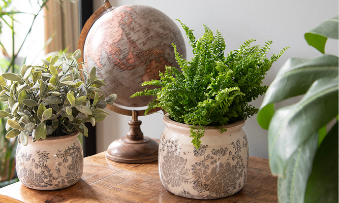 Ein Sideboard mit einem Vintage-Globus und zwei Shabby-Chic-Blumentöpfen mit Kunstpflanzen darin