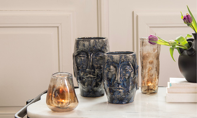 Des pots de fleurs bleu foncé avec un visage de l'île de Pâques et deux petits vases en verre marron