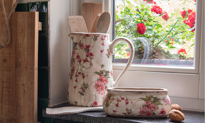 Een romantische schenkkan gevuld met houten keukengerei en ernaast staat een brede bloempot met walnoten