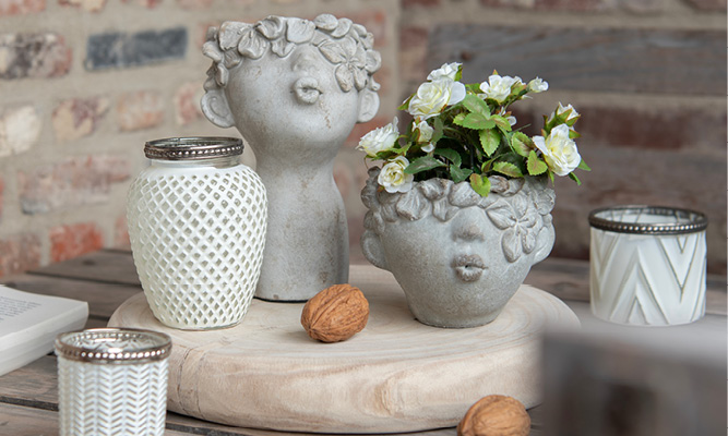 Due vasi per fiori in pietra con bambini che si baciano nell'aria e portacandele in vetro bianco su un vassoio di legno