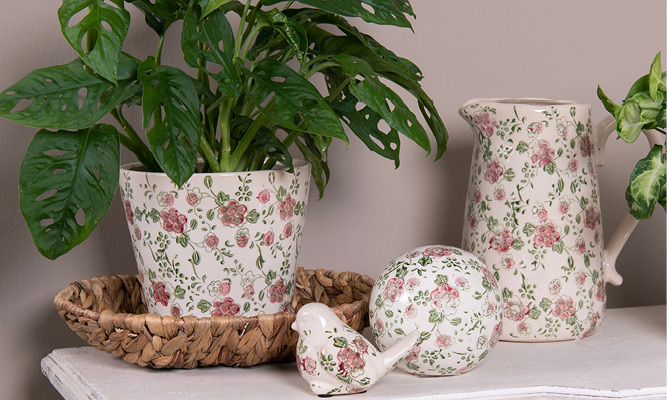 Una collezione di accessori per la casa romantici, tra cui un vaso per fiori, una brocca, una statuetta di uccello e una sfera decorativa con un motivo floreale rosa