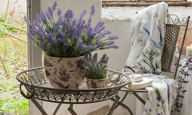 Zwei Lavendelblumentöpfe, gefüllt mit Lavendel, auf einem Pflanztisch aus Eisen mit einem Gartenstuhl aus Eisen und einer Decke