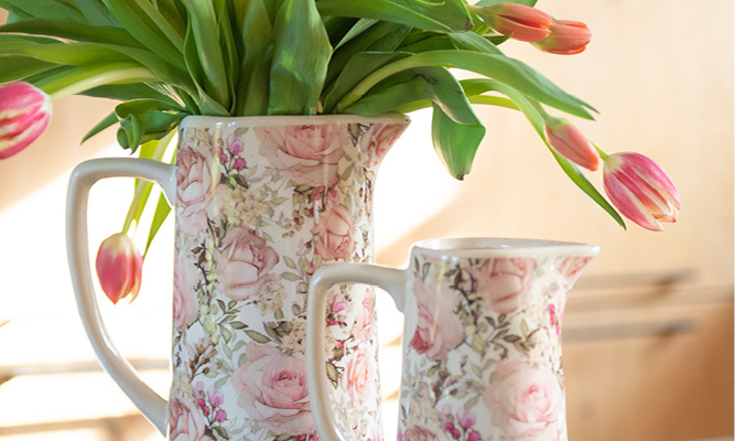 Eine dekorative Kanne bedeckt mit altmodischen Rosen und gefüllt mit rosa Tulpen