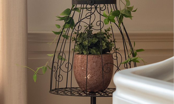 A black metal mannequin with a pink flower pot adorned with artificial branches inside