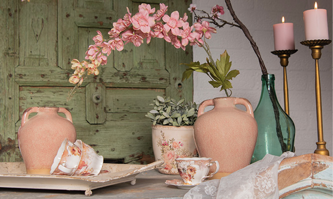 Ein romantischer Einrichtungsstil mit altmodischen Teetassen, hellrosa Vasen, Landhaus-Blumentöpfen und goldfarbenen Kerzenhaltern