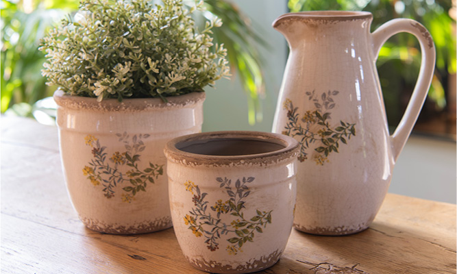 Two country-style flower pots with a branch of various wildflowers and a decorative pitcher with the same pattern