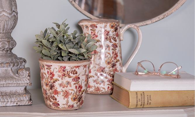 Un pot de fleurs à l'ancienne avec un motif floral antique, derrière se trouve une cruche décorative et à côté se trouvent deux vieux livres