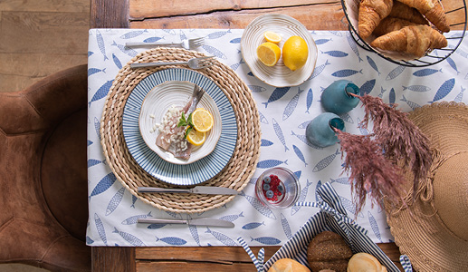 A summer table with a fish tablecloth and a served dish on a rattan placemat