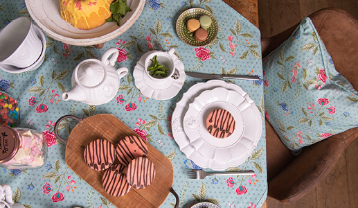 Ein fröhlich gedeckter Tisch für eine Teeparty mit einem blauen Tischtuch mit rosa Blumen und weißem romantischem Geschirr und rosa Kuchen