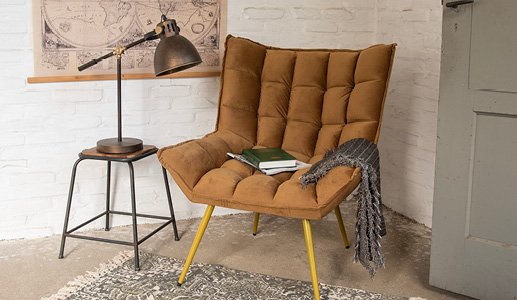 Ein industrielles Wohnambiente mit einem braunen Sessel und einer grauen Decke sowie einem Holz-Metall-Hocker mit einer industriellen Tischlampe