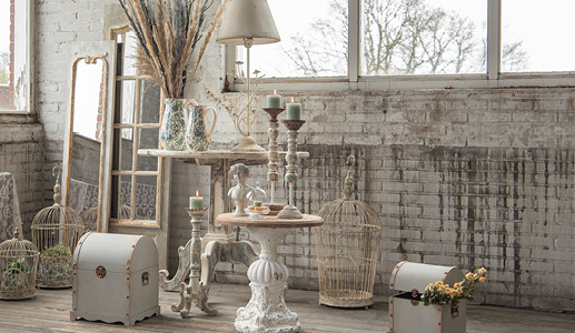 Een grote shabby chic woonstijl met diverse items, waaronder bijzettafels, kandelaren, vogelkooien, kisten, schenkkannen en droogbloemen