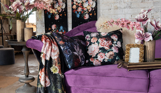 A purple couch in a dramatic style with cushions and throws featuring beautiful floral patterns