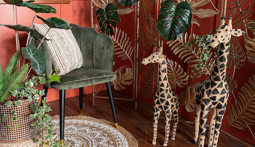 Een rode kamer met twee giraffen beelden en een groene stoel met een botanische sierkussen