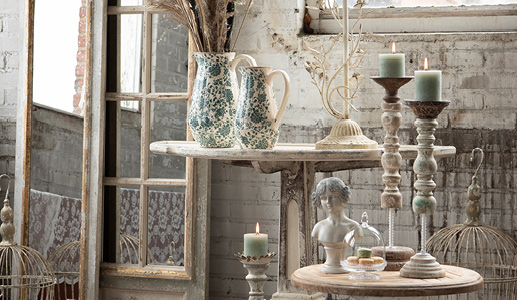 A shabby chic interior style with weathered candleholders, a bust of a girl, and two decorative pouring jugs with dried flowers