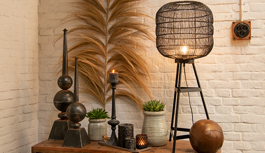 A cabinet filled with decorative items, including a black floor lamp, a leather decorative ball, gray flower pots, black candle holders, black figurines, and black tea light holders