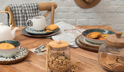 Een gedekte tafel in landelijke stijl met een krant en leesbril, met landelijke dinerborden en ontbijtborden en een witte mok