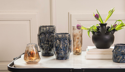 A marble coffee table with two dark blue flower pots featuring Easter Island heads, two beige vases, and a tulip vase filled with purple tulips