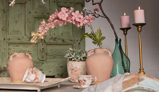 A romantic setting with pink and green vases, two gold candleholders, and vintage teacups and saucers