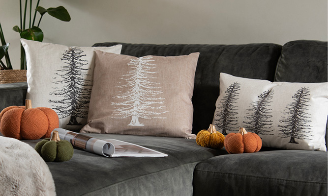 A gray couch with three decorative pillows featuring pine trees and fabric pumpkins