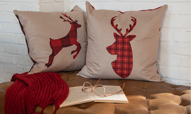 Twee beige kerstkussens met een hert erop met een rood klassiek geruit patroon